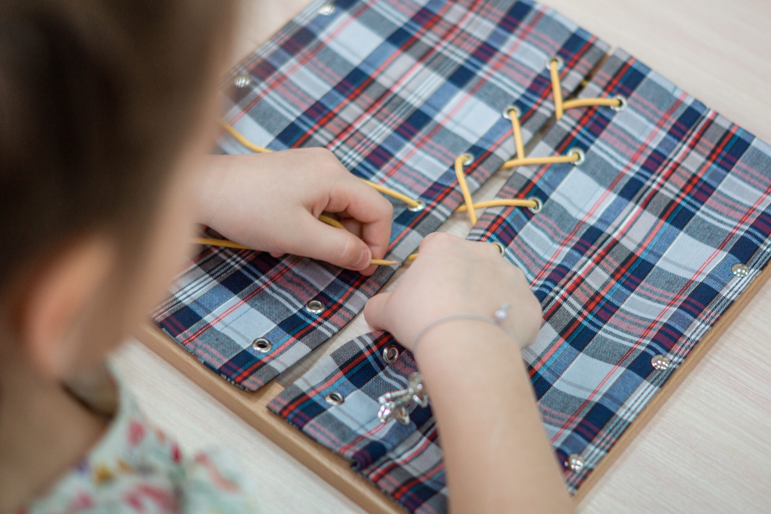 focused young child practicing fine motor skills with plaid lacing board
