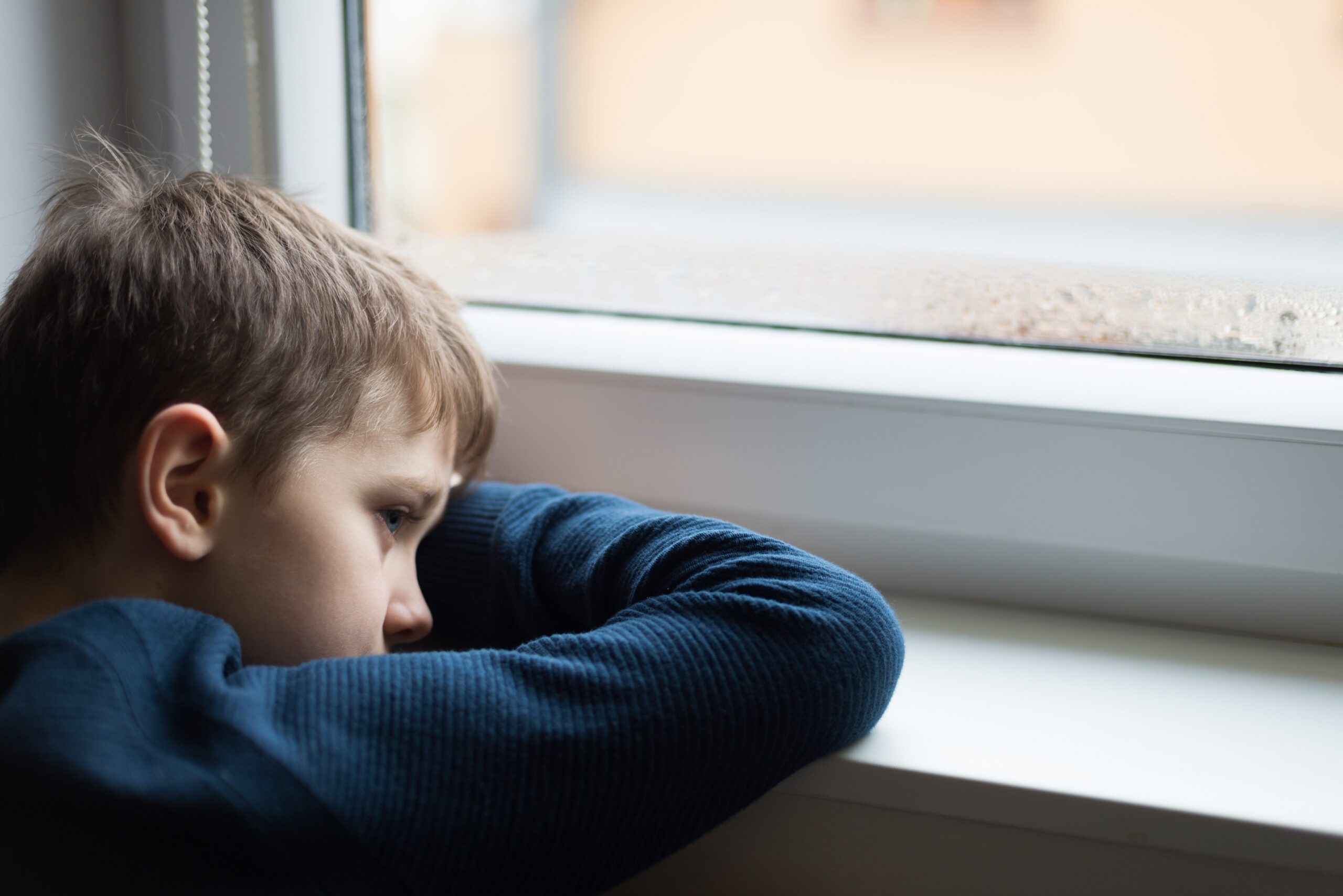Sad alone little boy child looking through the window
